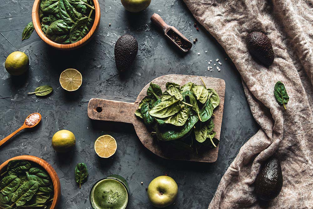 Healthy foods, cooking and vegetarian concept spinach leaves, lemon, apples, avocado, cutting board