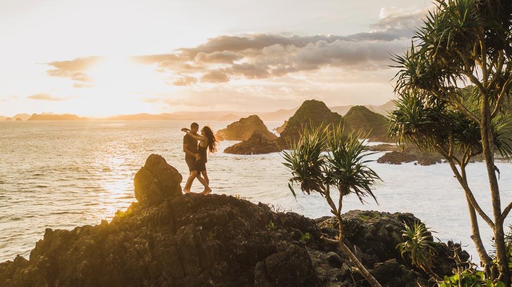 Couple enjoying sunset with amazing ocean and mountain view. Tra